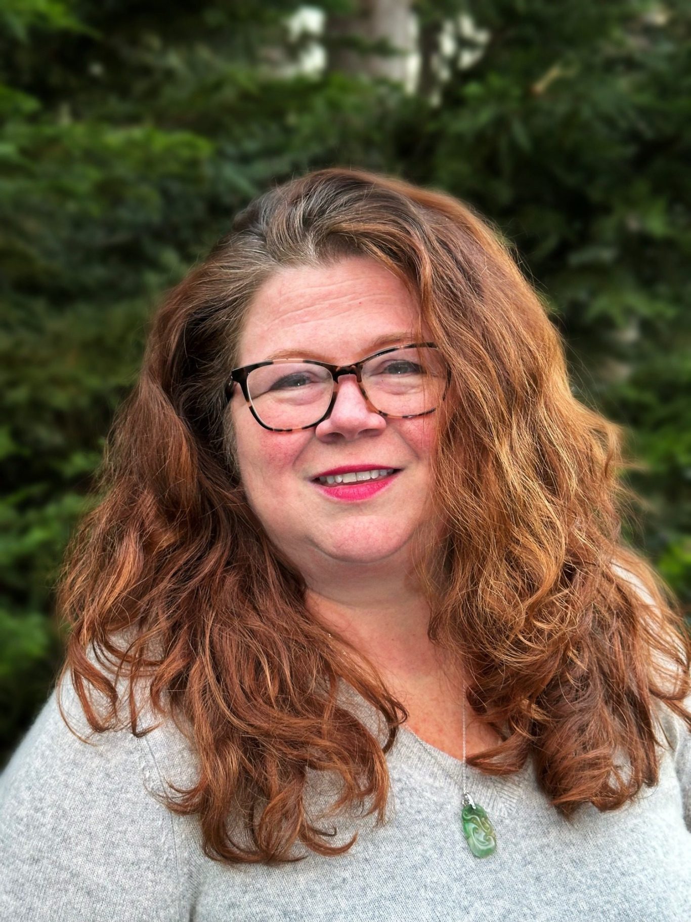 A white woman with red hair and glasses wearing a gray sweater